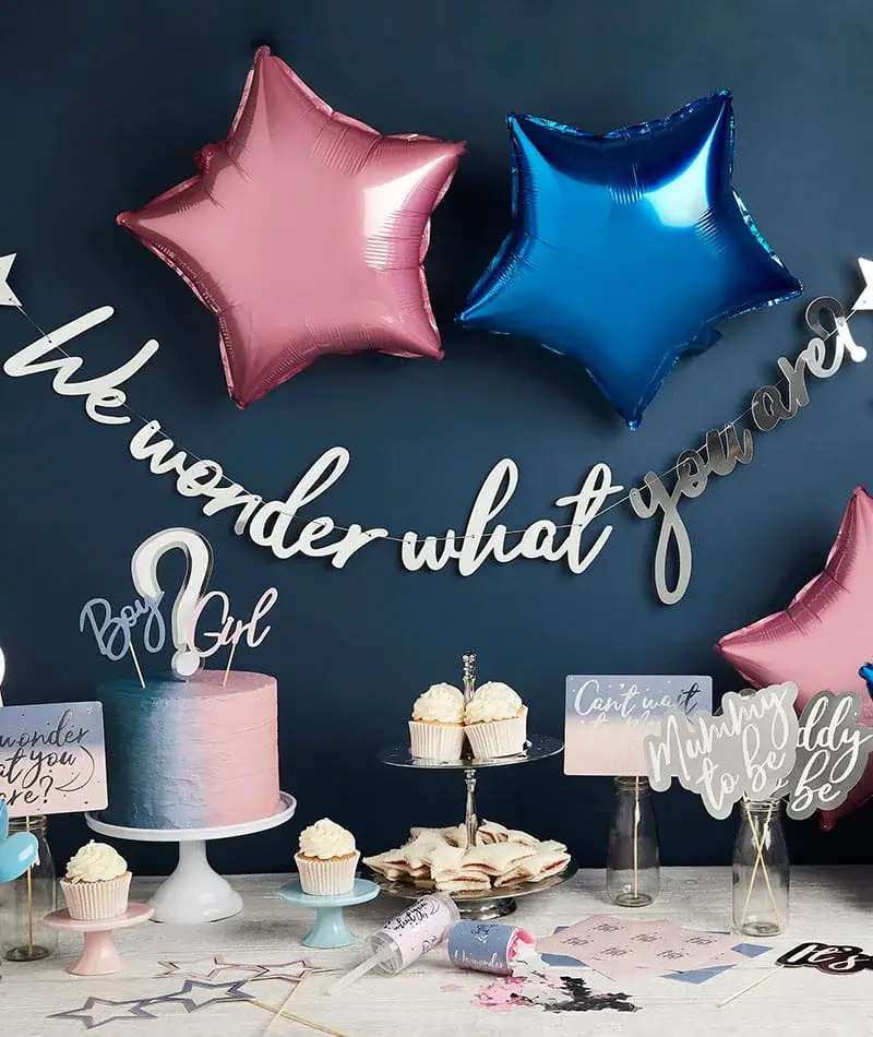 Gender reveal party display with pink and blue star balloons, a pastel cake, cupcakes, and themed decorations on a dessert table. Gender reveal party display with pink and blue star balloons, a pastel cake, cupcakes, and themed decorations on a dessert table.